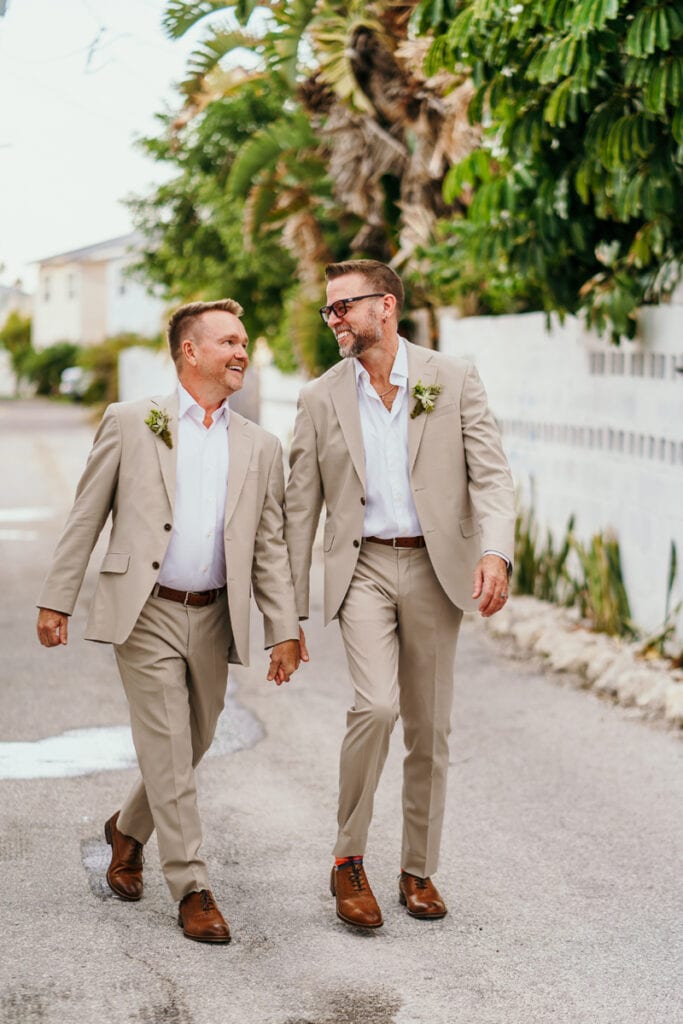 Wedding Photographer, two newly married husbands walk together smiling on the street
